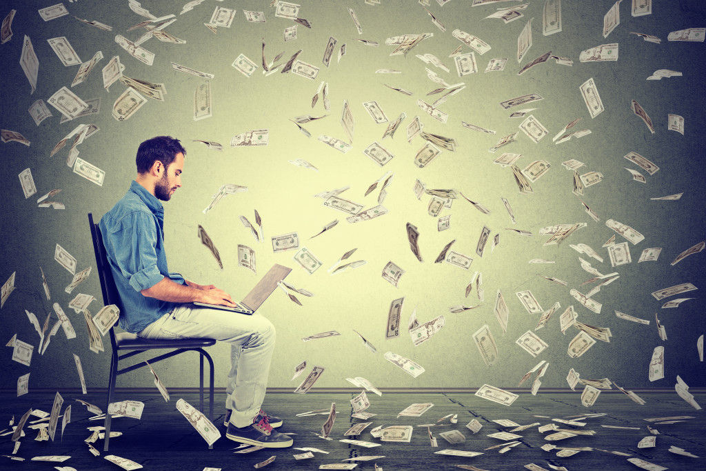 man on a laptop with money falling like confetti around him