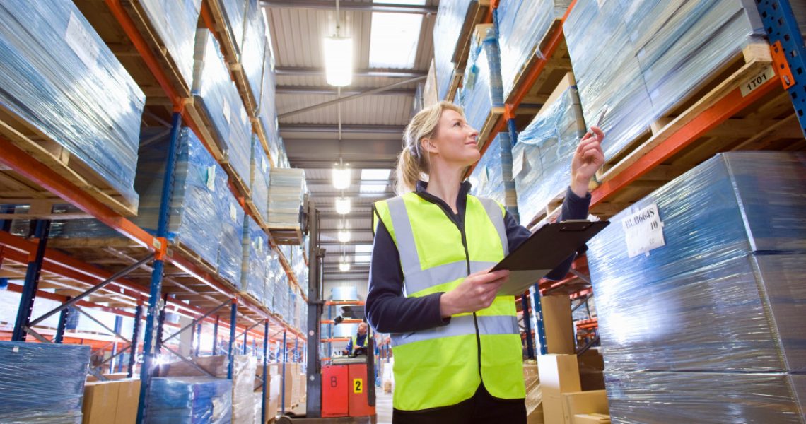 A low angle medium shot of a female warehouse worker holding a clipboard and checking inventory.